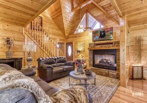 A log cabin interior with a fireplace, a sofa, a coffee table, and a television mounted above the fireplace. - Secluded 4BR Cabin - Hot tub & Game Room - Smokies (Sevierville)