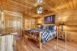 A wooden cabin bedroom with a bed, two bedside tables, a ceiling fan, and a painting on the wall. - Secluded 4BR Cabin - Hot tub & Game Room - Smokies (Sevierville)