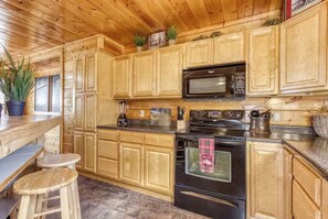 A kitchen with wooden cabinets, a microwave, a stove, and a bar area with stools. - Secluded 4BR Cabin - Hot tub & Game Room - Smokies (Sevierville)