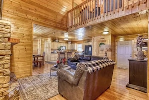 A log cabin interior with a living room, dining area, kitchen, and a loft bedroom. - Secluded 4BR Cabin - Hot tub & Game Room - Smokies (Sevierville)