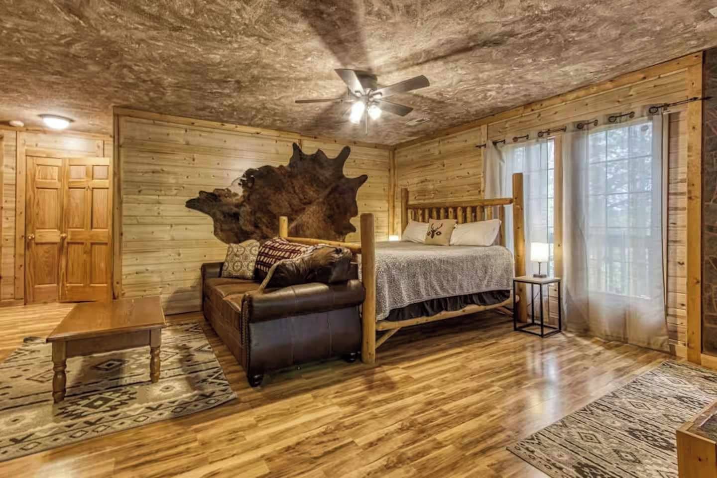 Un dormitorio tipo cabaña de madera con una cama con dosel, un banco de madera, una mesita y una decoración de gran tronco de árbol.