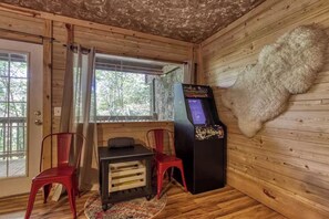 A room with wooden walls, a fur rug, a table with chairs, and a claw machine. - Inviting 1BR Cabin - Hot tub & Fireplace - Smokies (Sevierville)