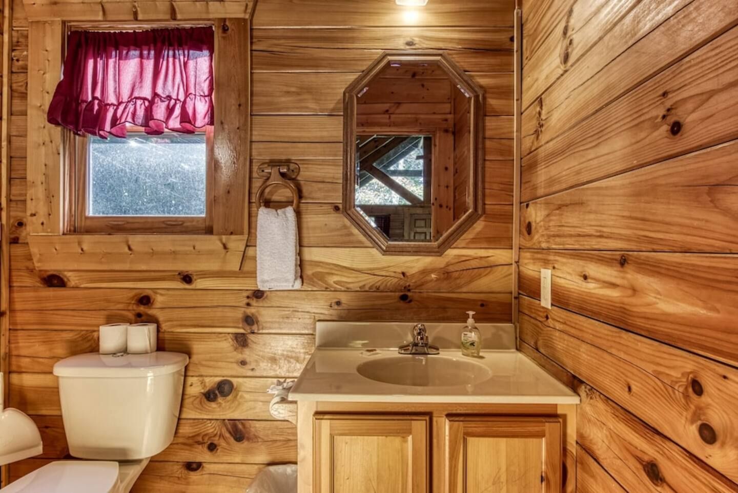 A wooden cabin bathroom with a toilet, sink, and window.