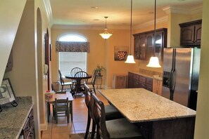 Una cocina con encimeras de granito, refrigerador de acero inoxidable y gabinetes de madera.
