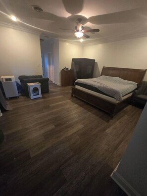 Un dormitorio con cama, ventilador de techo, calefactor y una mesita.