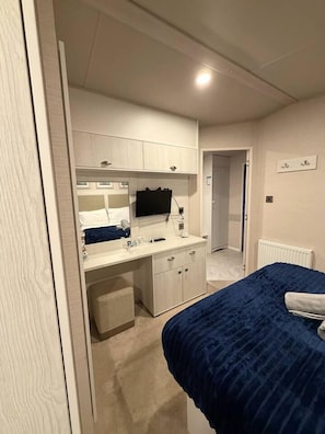 A bedroom with a bed, a bedside table, a dresser, a mirror, and a television.