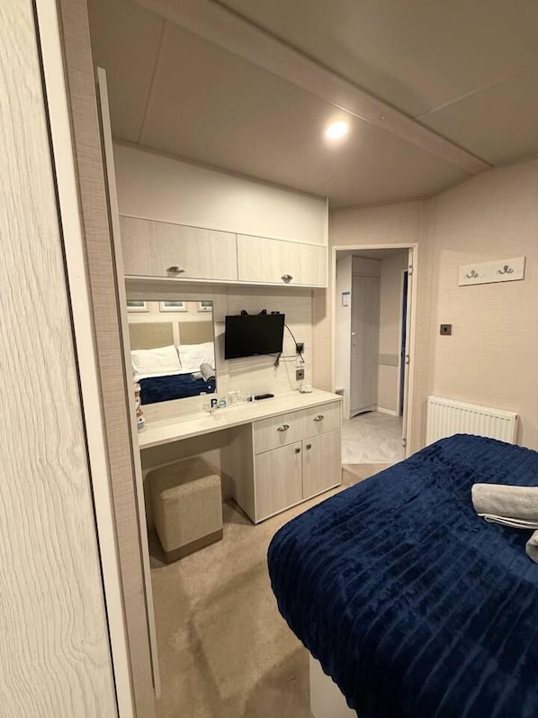 A bedroom with a bed, a bedside table, a dresser, a mirror, and a television.