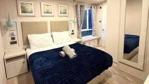 Un dormitorio con cama, mesitas de noche, un espejo y obras de arte en la pared.