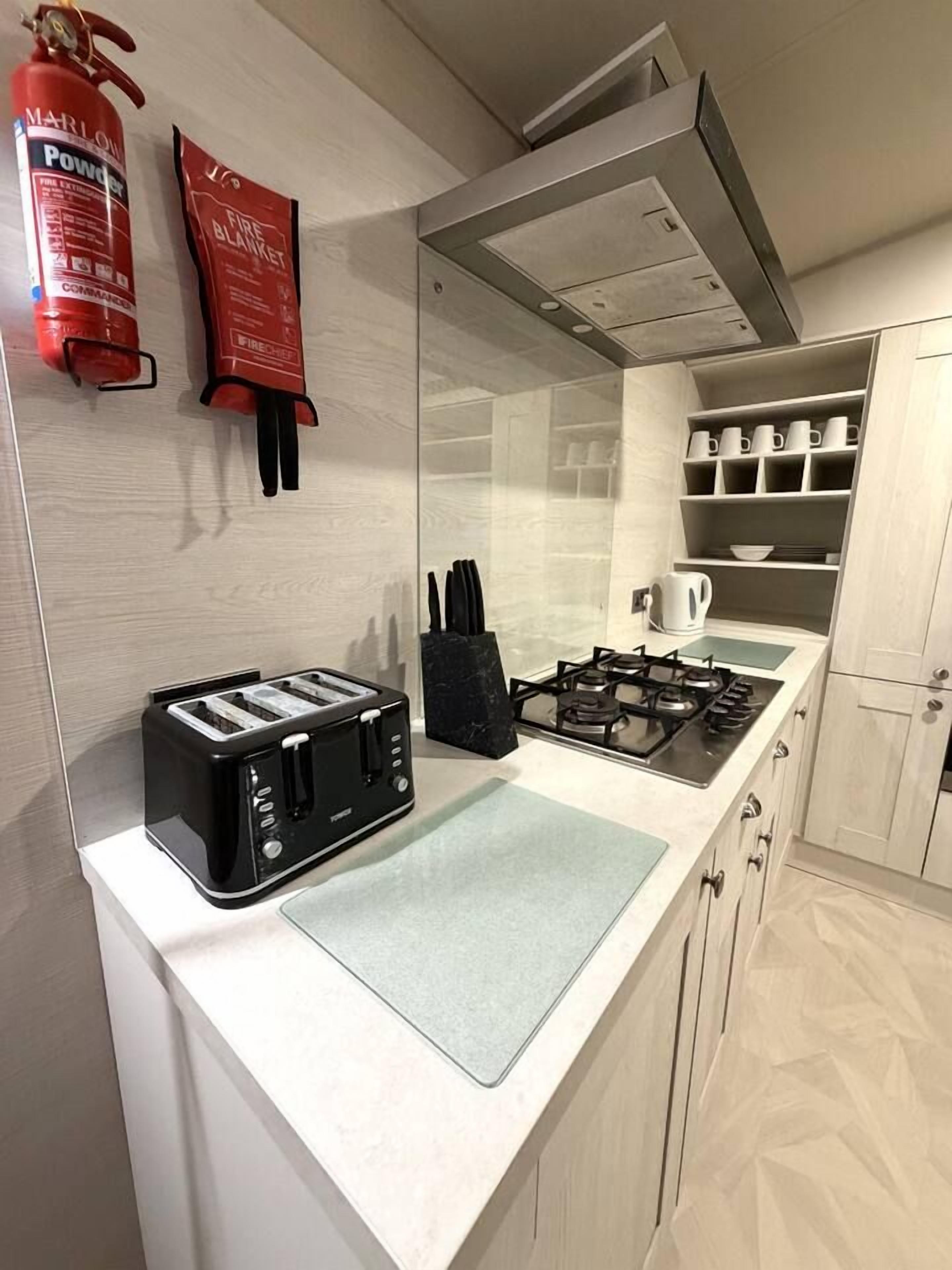 A kitchen with a toaster, a gas stove, a fire blanket, and a fire extinguisher.