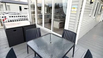A covered outdoor area with a table and chairs, a sliding glass door, and a white fence.