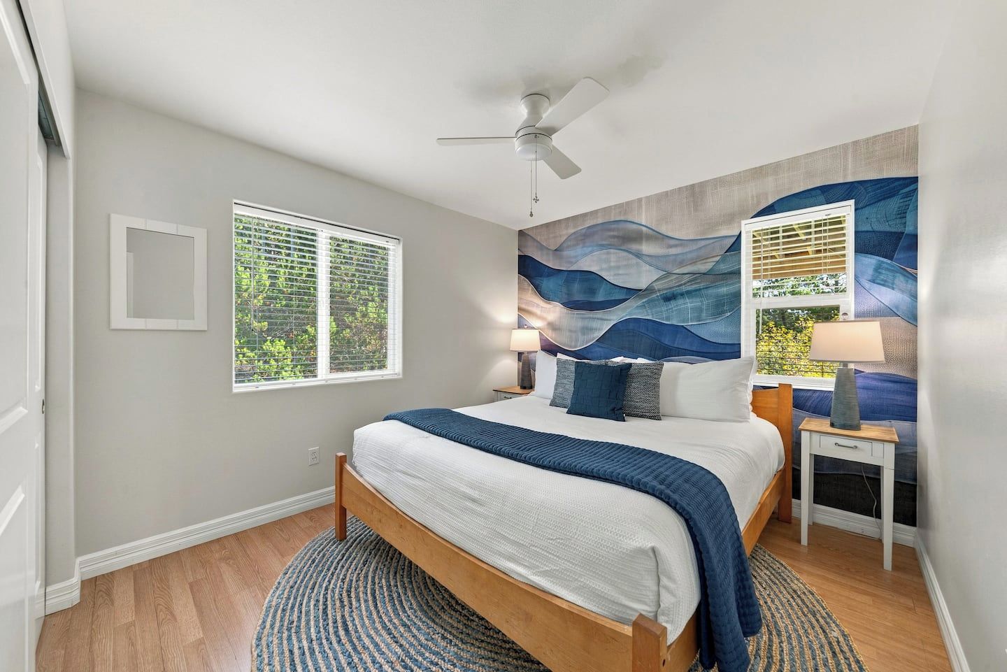 Une chambre à coucher comprenant un lit, un ventilateur de plafond, une fenêtre avec des stores, un climatiseur fixé au mur et une table de chevet avec une lampe.