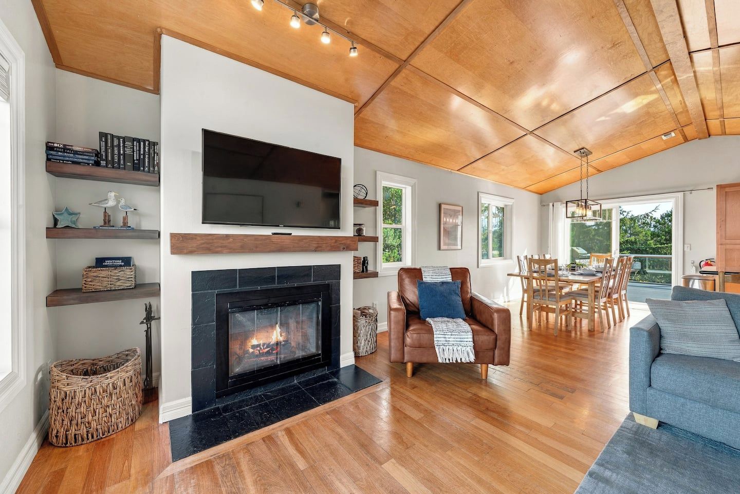 A spacious living room with a fireplace, wooden flooring, a leather armchair, and a dining area with natural light.