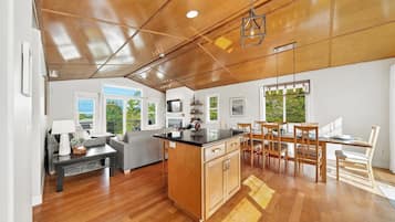 A modern kitchen with wooden cabinetry, a dining area with a wooden table and chairs, and a large window providing a view of greenery outside.