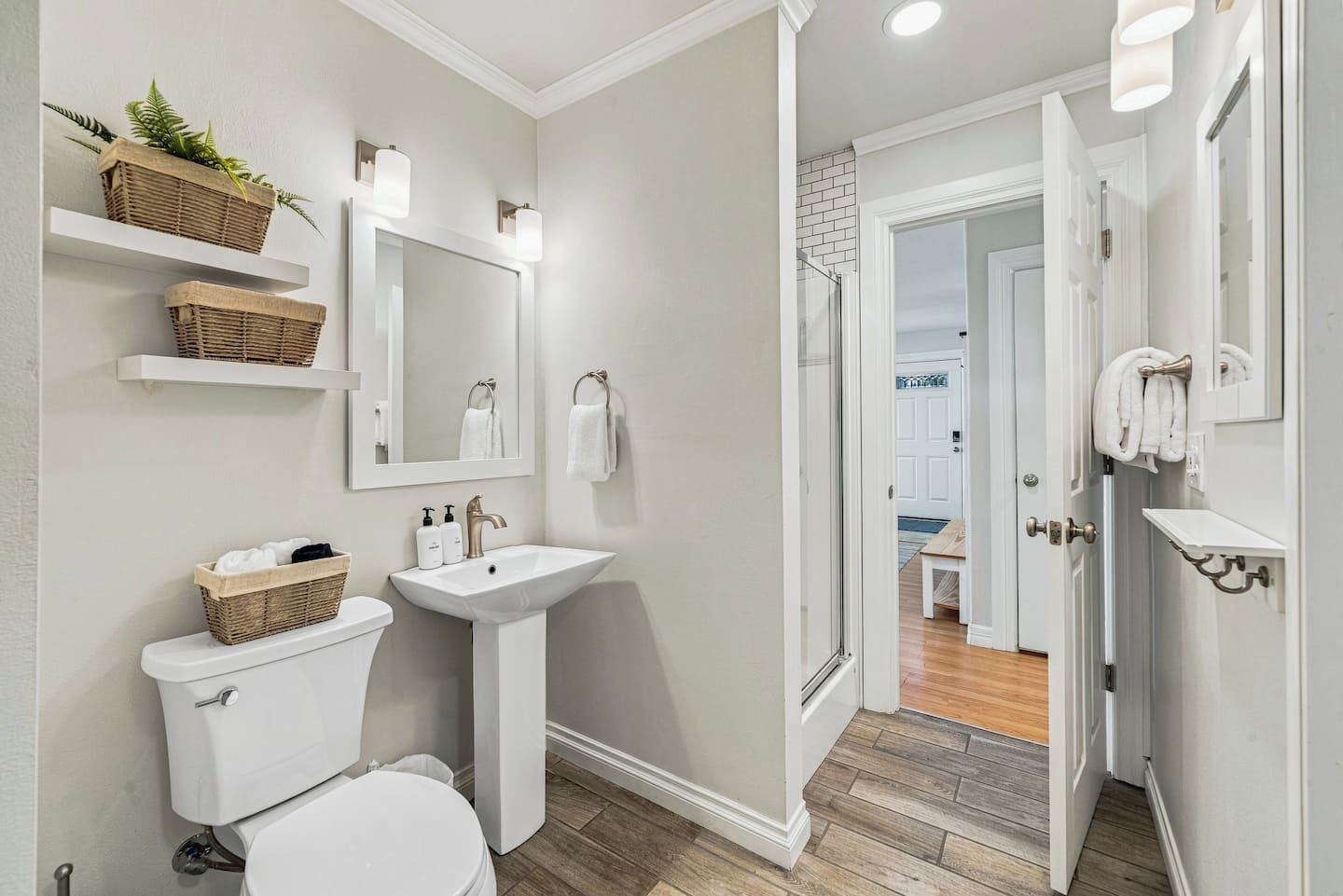 Une salle de bain moderne avec des toilettes, un lavabo et un miroir. On y trouve des étagères avec des paniers et des serviettes.