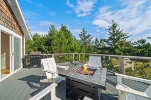 An outdoor deck with a grill, two chairs, and a table with a fire feature. - Sunset Crest | Game Room, Walk to Beach & Town (Manzanita)