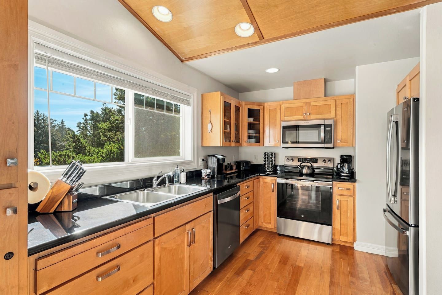 A modern kitchen with wooden cabinets, stainless steel appliances, and a large window.