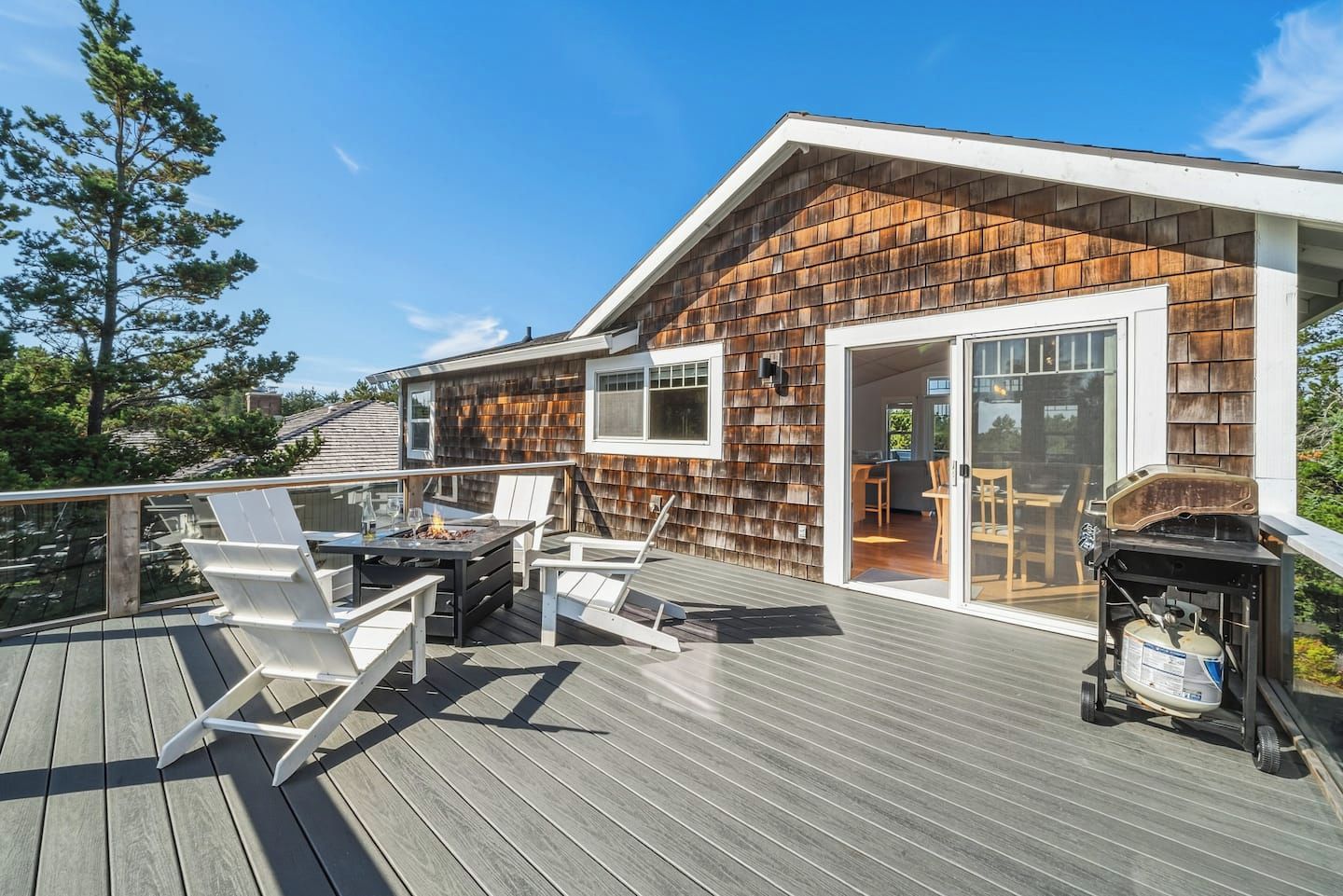 Una terraza con mobiliario exterior, una parrilla y un cerramiento de vidrio corredizo que da a un espacio interior.