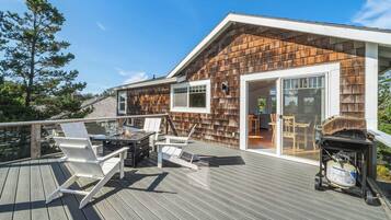 Una terraza con mobiliario exterior, una parrilla y un cerramiento de vidrio corredizo que da a un espacio interior.