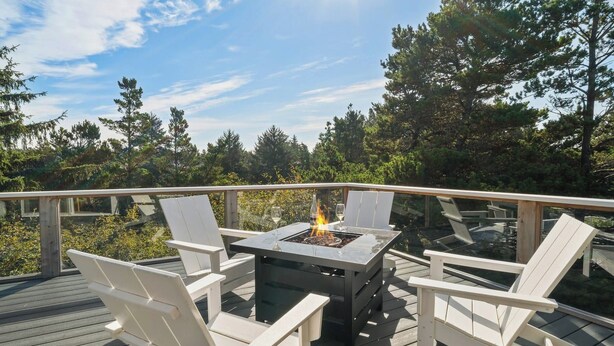Una terraza con mesa de vidrio, sillas blancas y una chimenea.