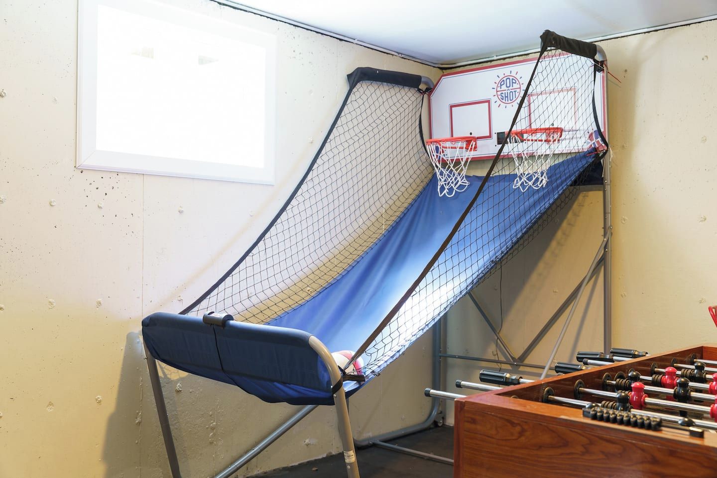 Une pièce d’angle avec un panier de basket, une fenêtre et une table de baby-foot.