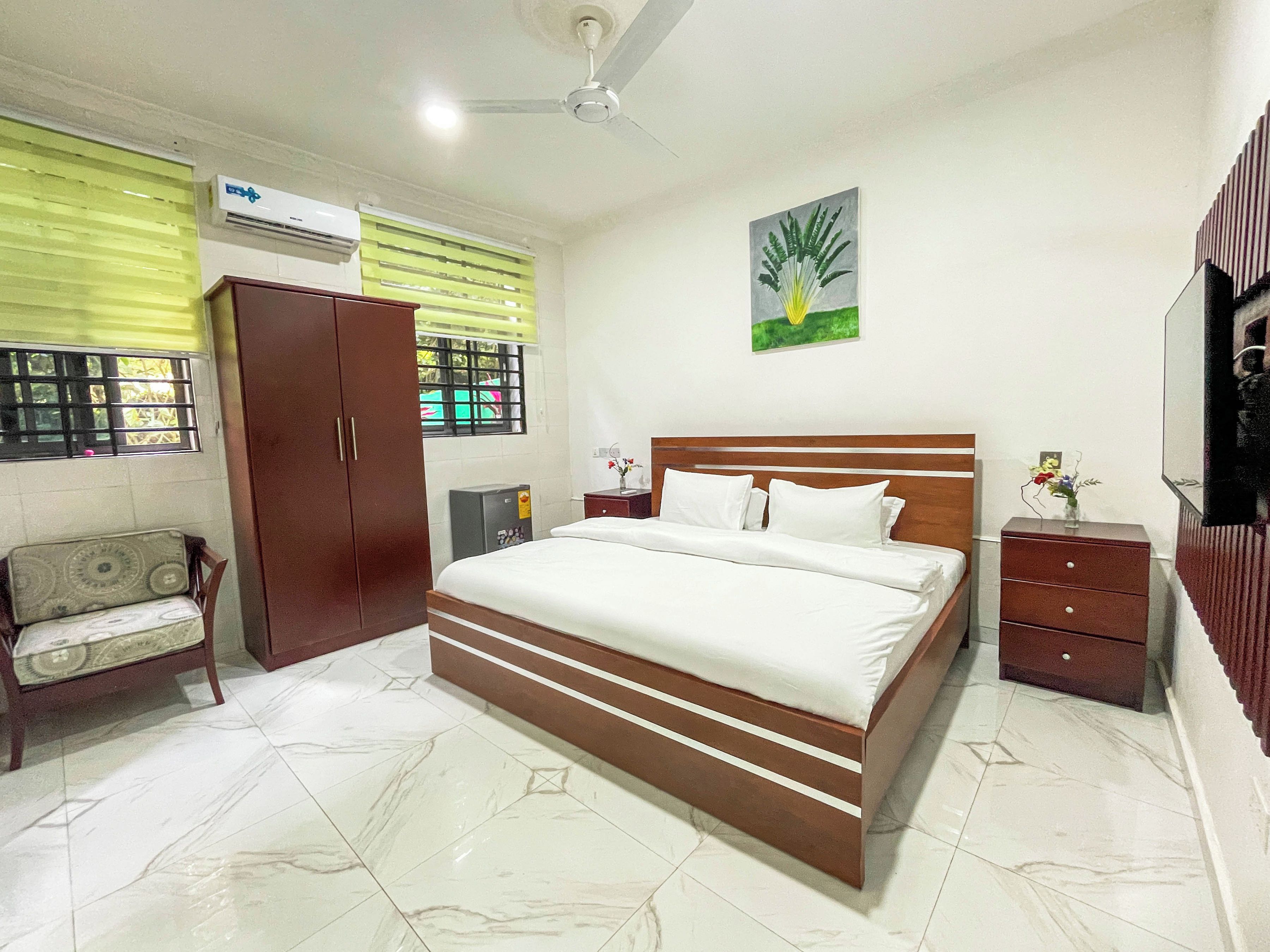 Un dormitorio con cama, armario, mesita de noche, espejo y ventana con persianas.