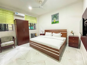 A bedroom with a bed, a wardrobe, a nightstand, a mirror, and a window with blinds.