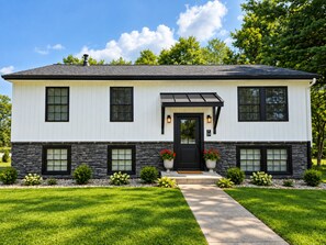 Une maison à deux étages avec une porte noire, un revêtement extérieur blanc et des éléments décoratifs en pierre.