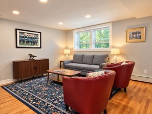 Un salon avec un canapé gris, des fauteuils rouges, une table basse en bois, un tapis à motifs et un meuble.