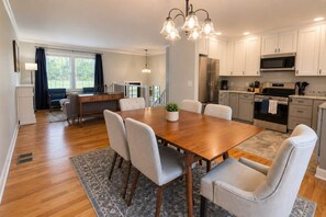 Une cuisine moderne avec des armoires blanches, des appareils en acier inoxydable et un coin repas comprenant une table et des chaises en bois.