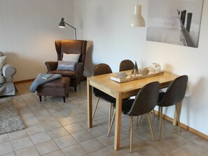 A dining area with a wooden table, black chairs, a brown leather chair with a pillow, a floor lamp, and a wall-mounted light fixture. - Holiday Apartment With 1 Bedroom (Hasselberg)