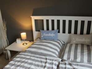 A hotel room with a bed, two pillows with text, a bedside table with a lamp, and a vase with plants. - Holiday Apartment With 1 Bedroom (Hasselberg)