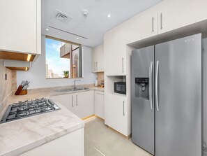 A modern kitchen with stainless steel appliances, white cabinetry, and a marble countertop. - Kensington Iconic Burj View Dubai Mall (Dubai)