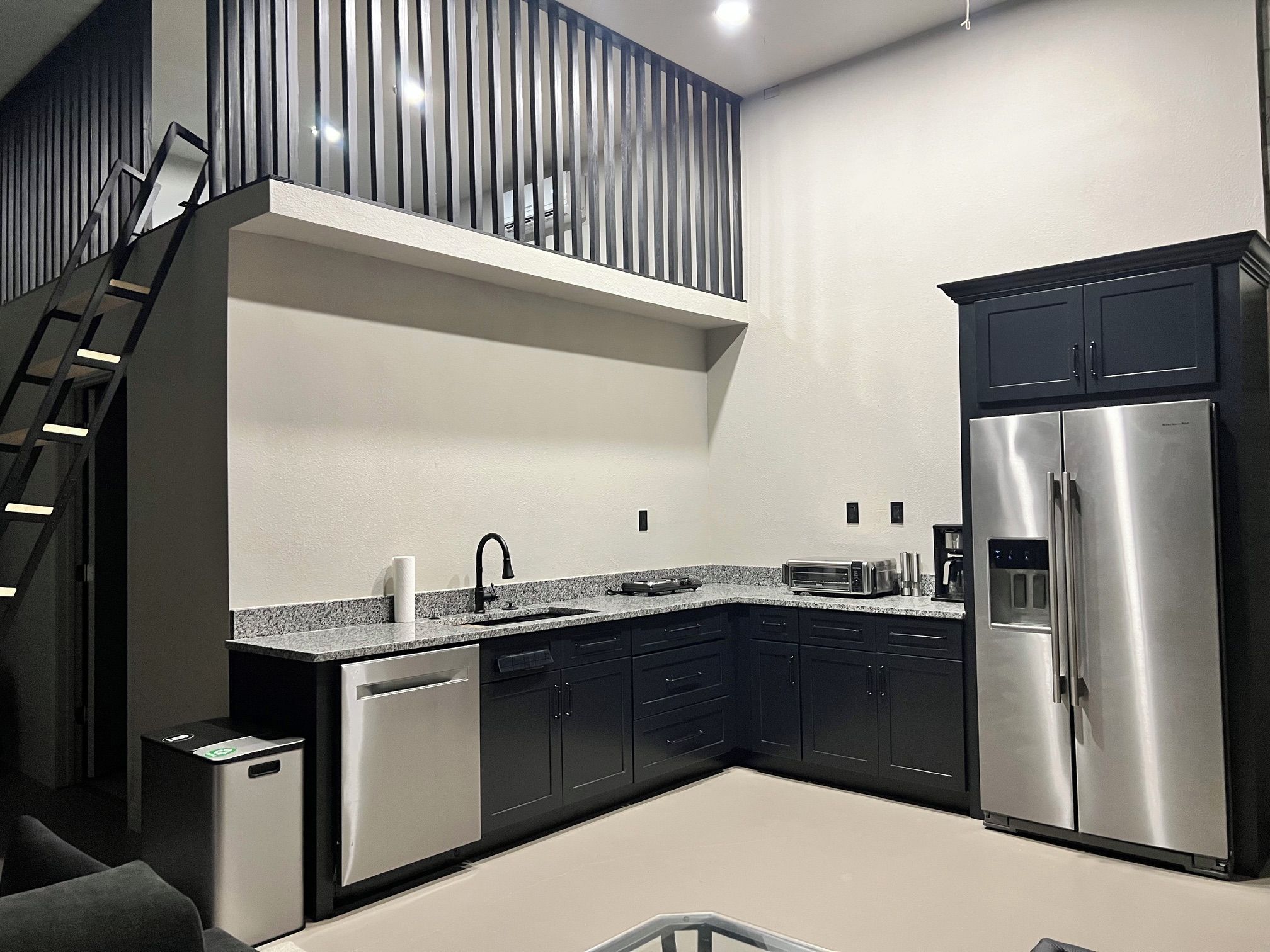 A modern kitchen with a stainless steel refrigerator, dark cabinetry, and a granite countertop.