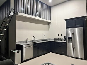 A modern kitchen with a stainless steel refrigerator, dark cabinetry, and a granite countertop. - Modern industrial guest suite in the heart of downtown Melbourne (Melbourne)