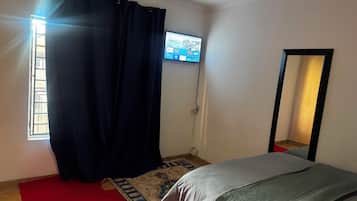 A bedroom with a bed, a television mounted on the wall, a window with curtains, and a mirror.