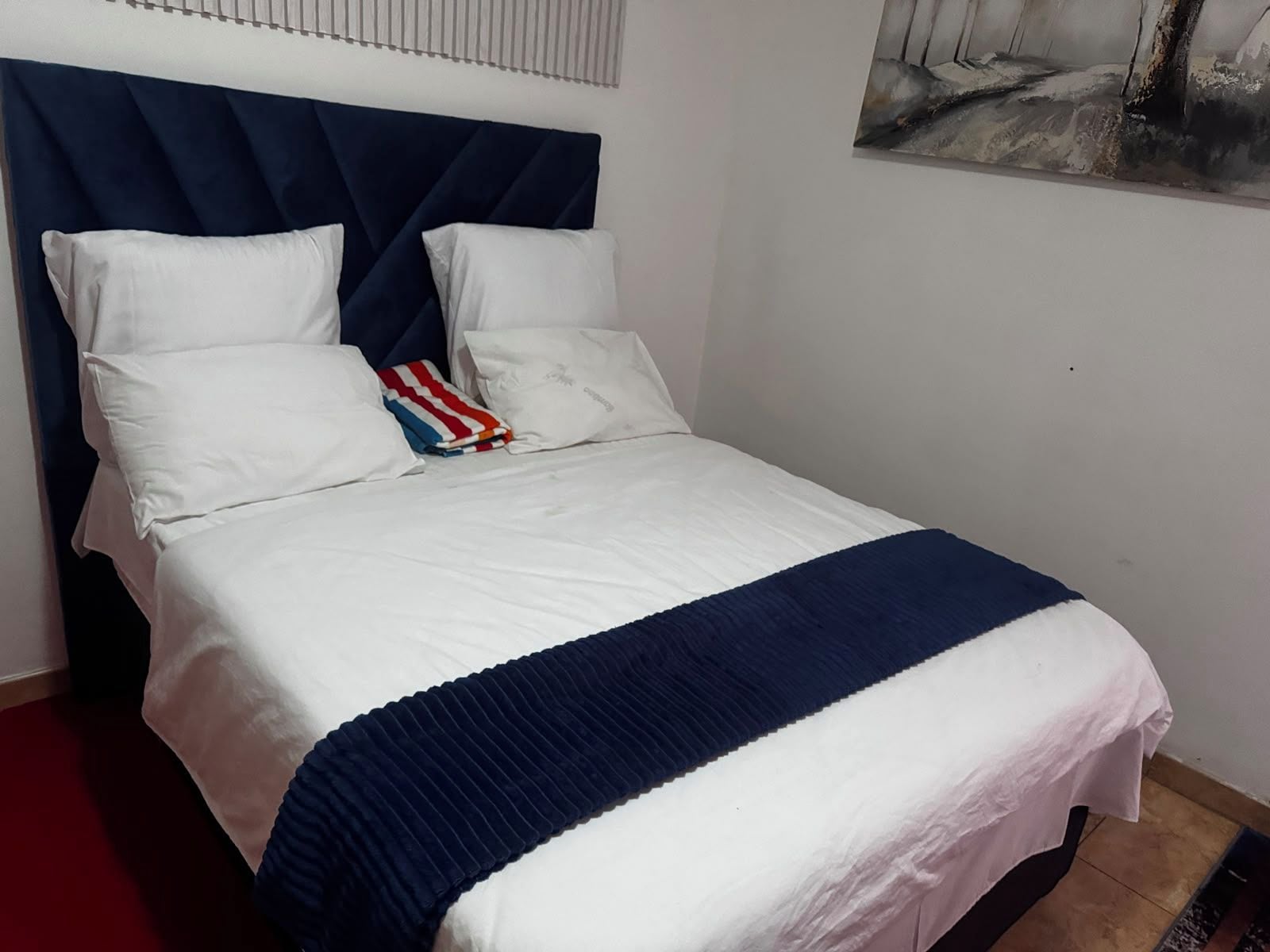 A bed with a white and blue striped bedspread, a dark blue headboard, and white pillows.
