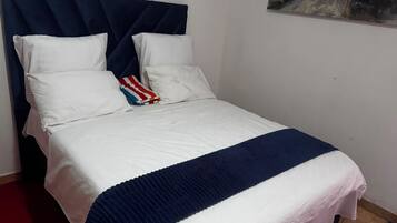 A bed with a white and blue striped bedspread, a dark blue headboard, and white pillows.