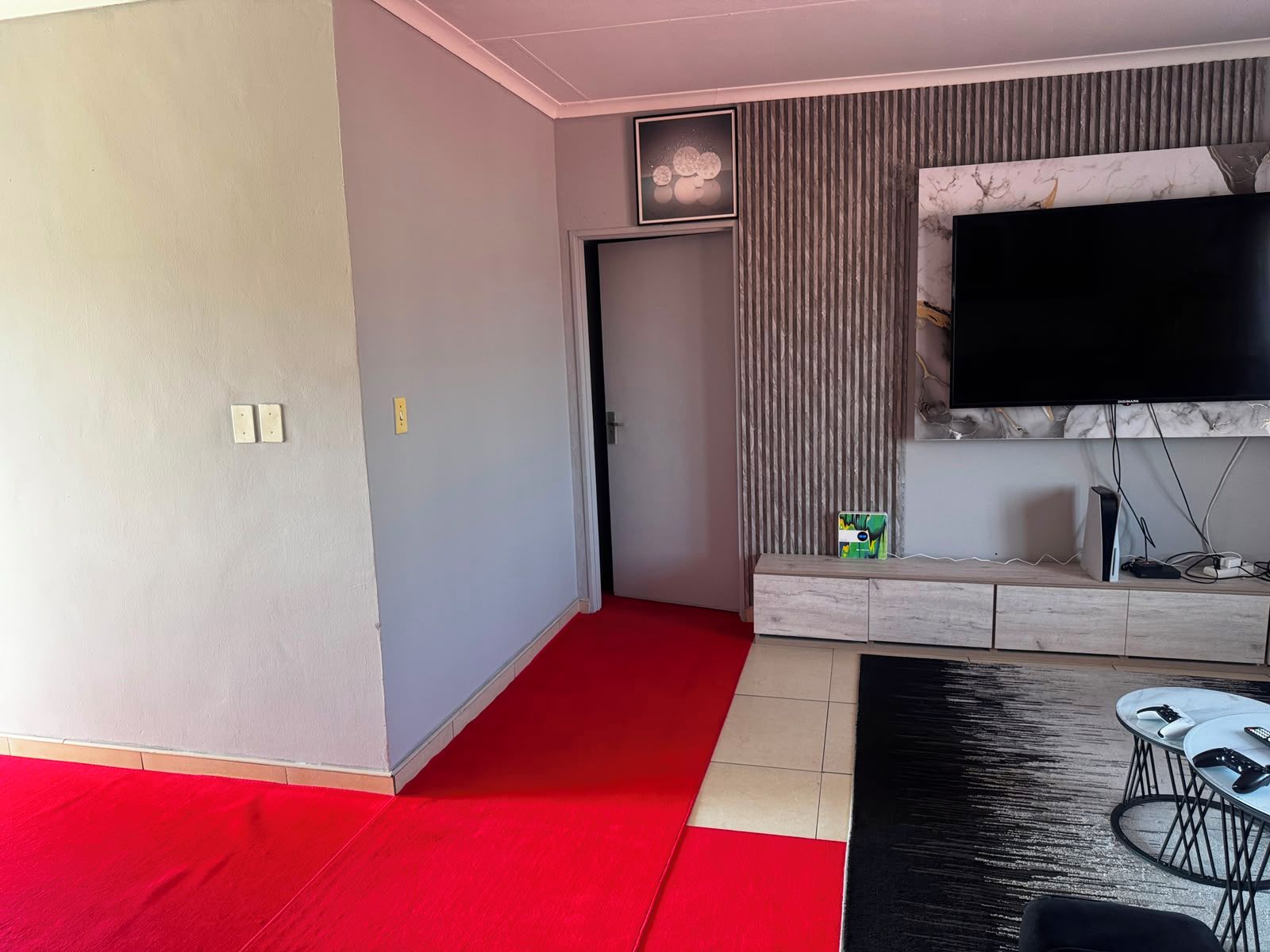 A modern living room with a flat-screen TV mounted on the wall, a wooden entertainment unit, and a red carpeted area.
