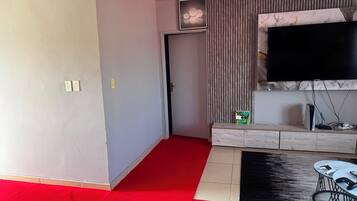A modern living room with a flat-screen TV mounted on the wall, a wooden entertainment unit, and a red carpeted area.
