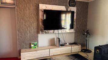 A modern living room with a flat-screen TV mounted on a marble wall, a wooden entertainment unit below, a black and white rug, and a black suitcase.