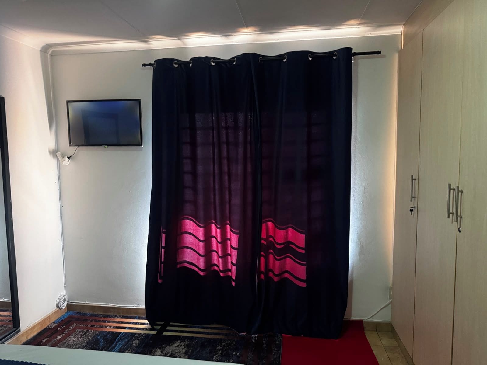 A room with a black curtain, a flat-screen TV mounted on the wall, and a red carpet on the floor.