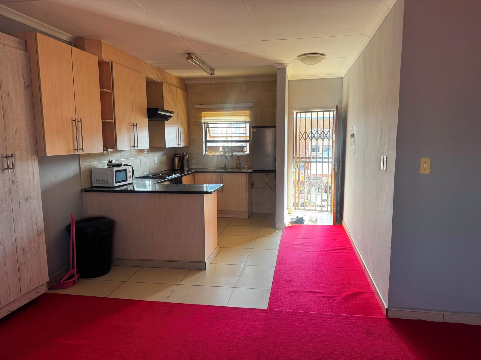 A kitchen with wooden cabinets, a microwave, and a red carpet leading to an open door.