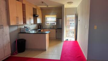 A kitchen with wooden cabinets, a microwave, and a red carpet leading to an open door.