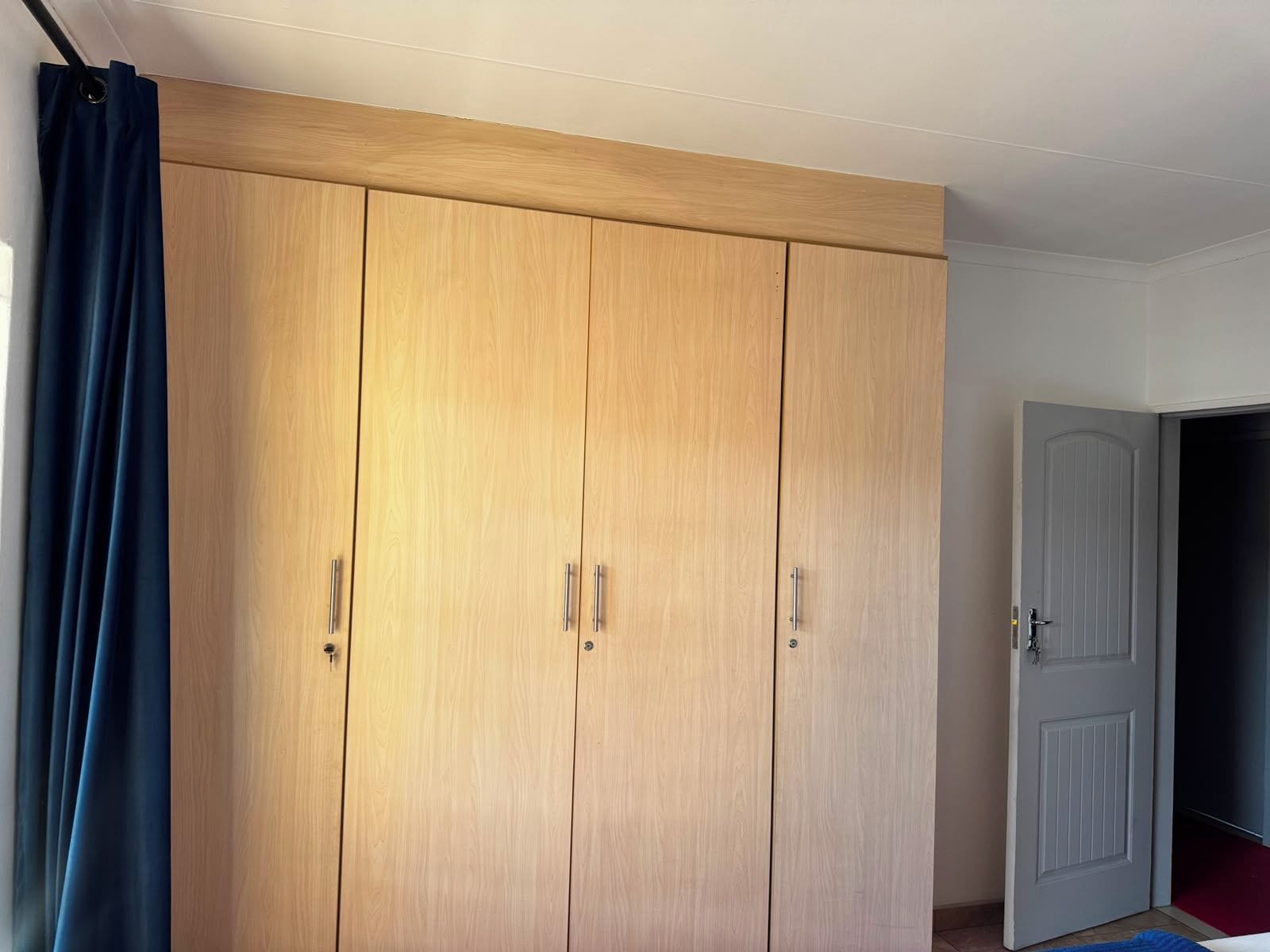 Une pièce avec une grande armoire en bois, une porte et un rideau bleu.