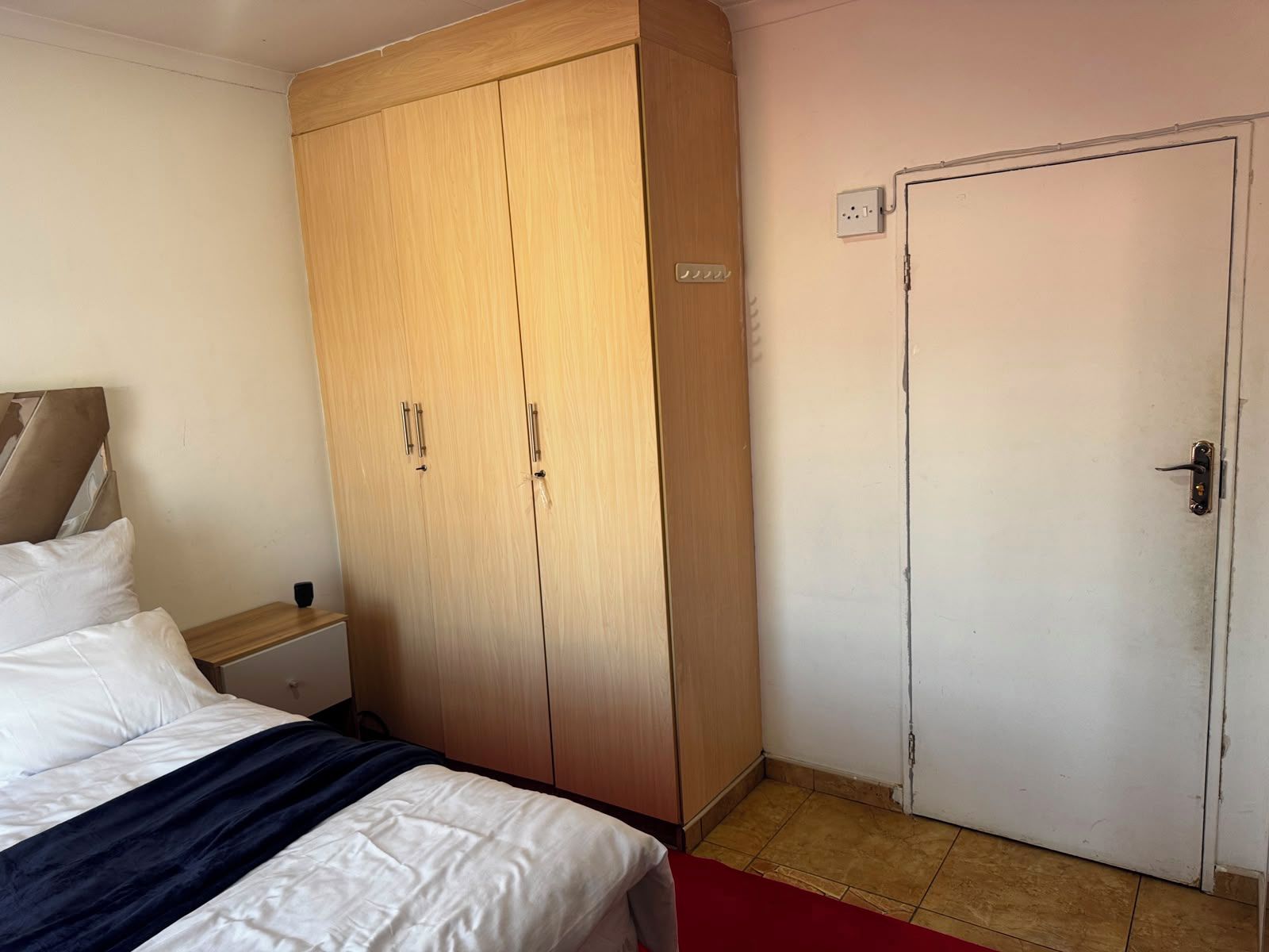 A bedroom with a bed, a wardrobe, a nightstand, and a door.