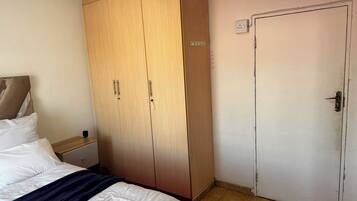 A bedroom with a bed, a wardrobe, a nightstand, and a door.