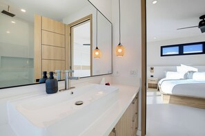 Ein modernes Badezimmer mit einem großen Spiegel, einem weißen Waschbecken und zwei Pendelleuchten.