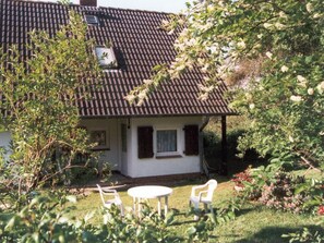 Ein Haus mit einem Ziegeldach, einer kleinen Veranda und einem Garten mit Stühlen und Pflanzen.