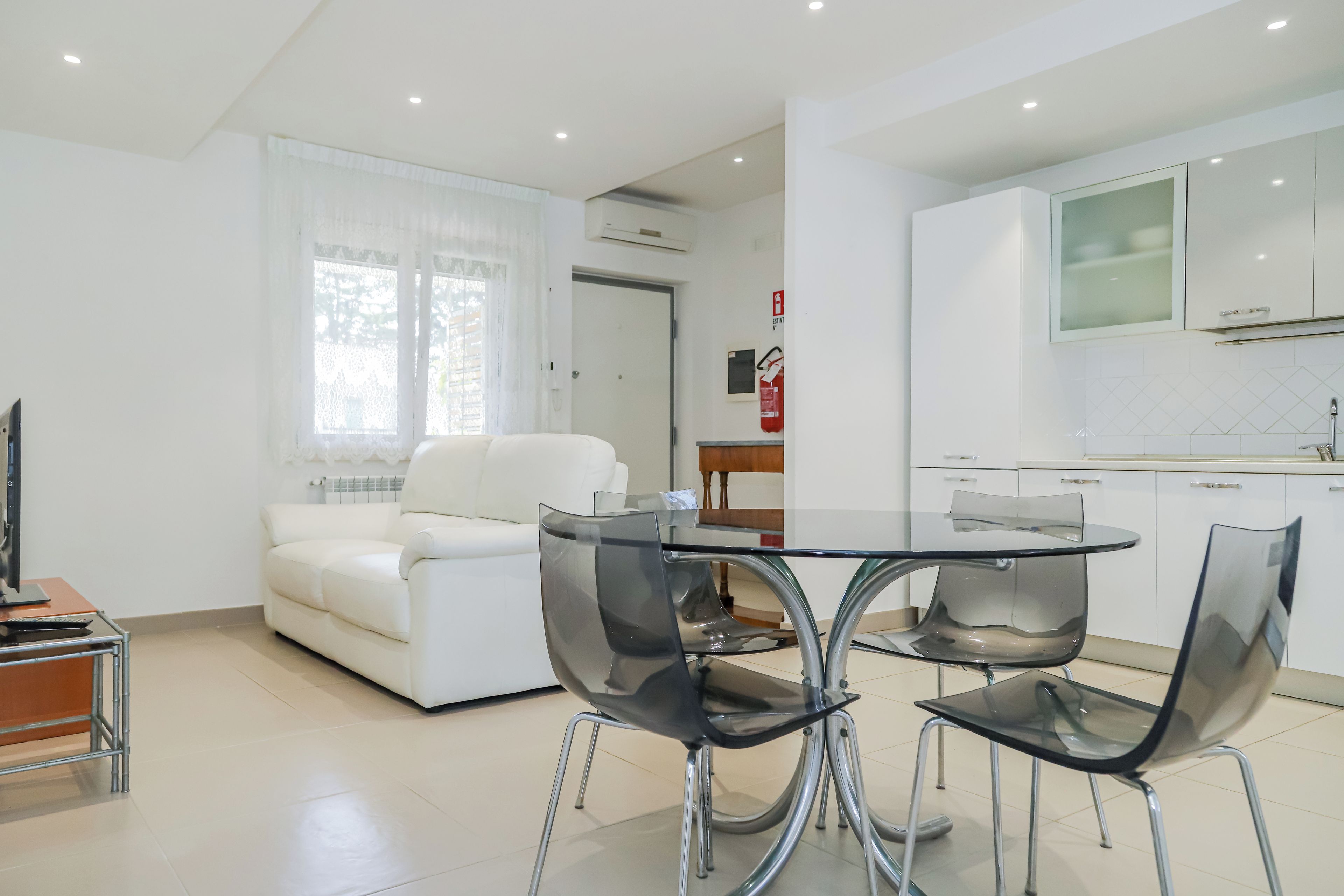 A modern living room with a white sofa, a glass coffee table, and black chairs.