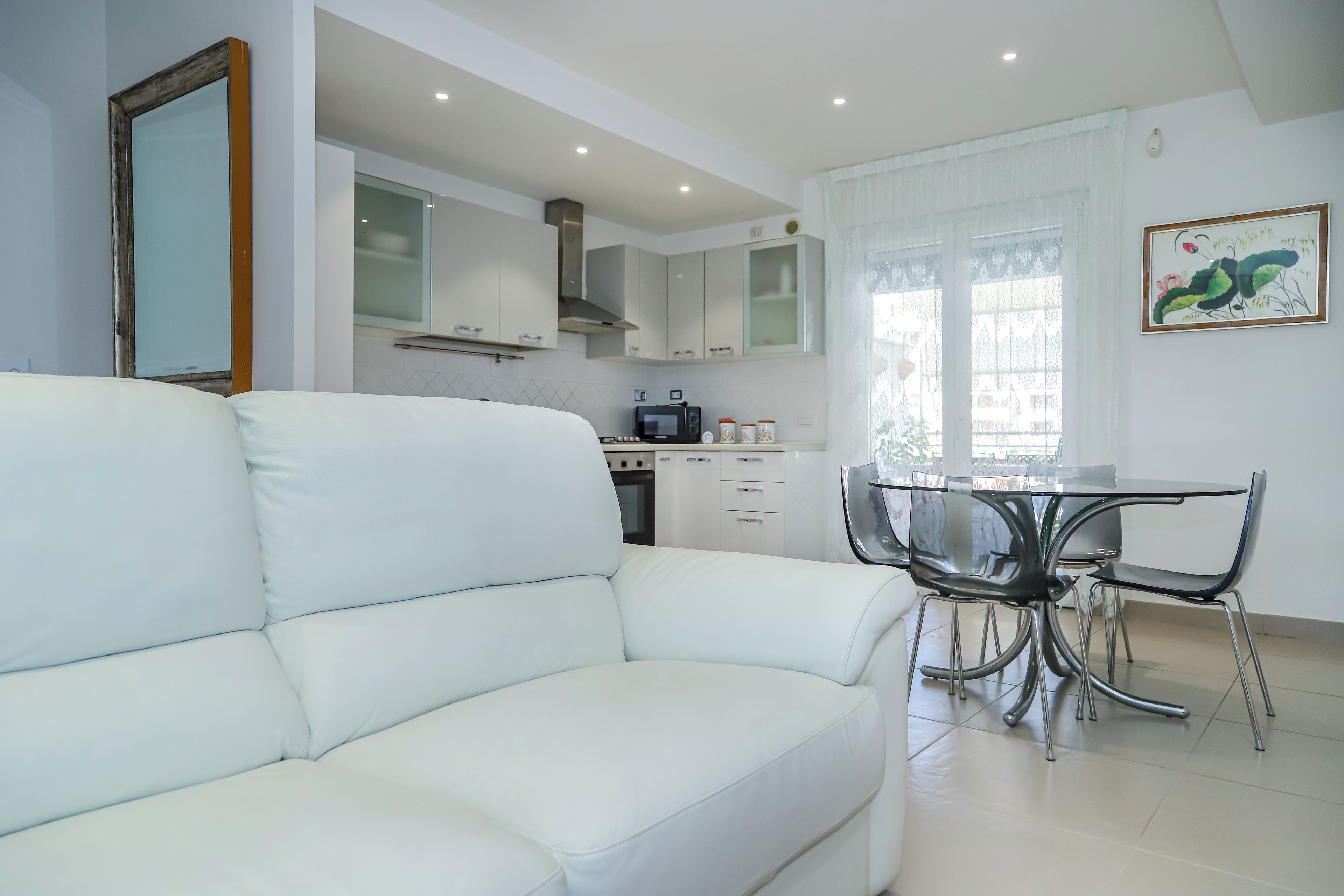 Una cocina moderna con armarios blancos, una mesa de comedor con sillas y un sofá blanco en una sala de estar luminosa.